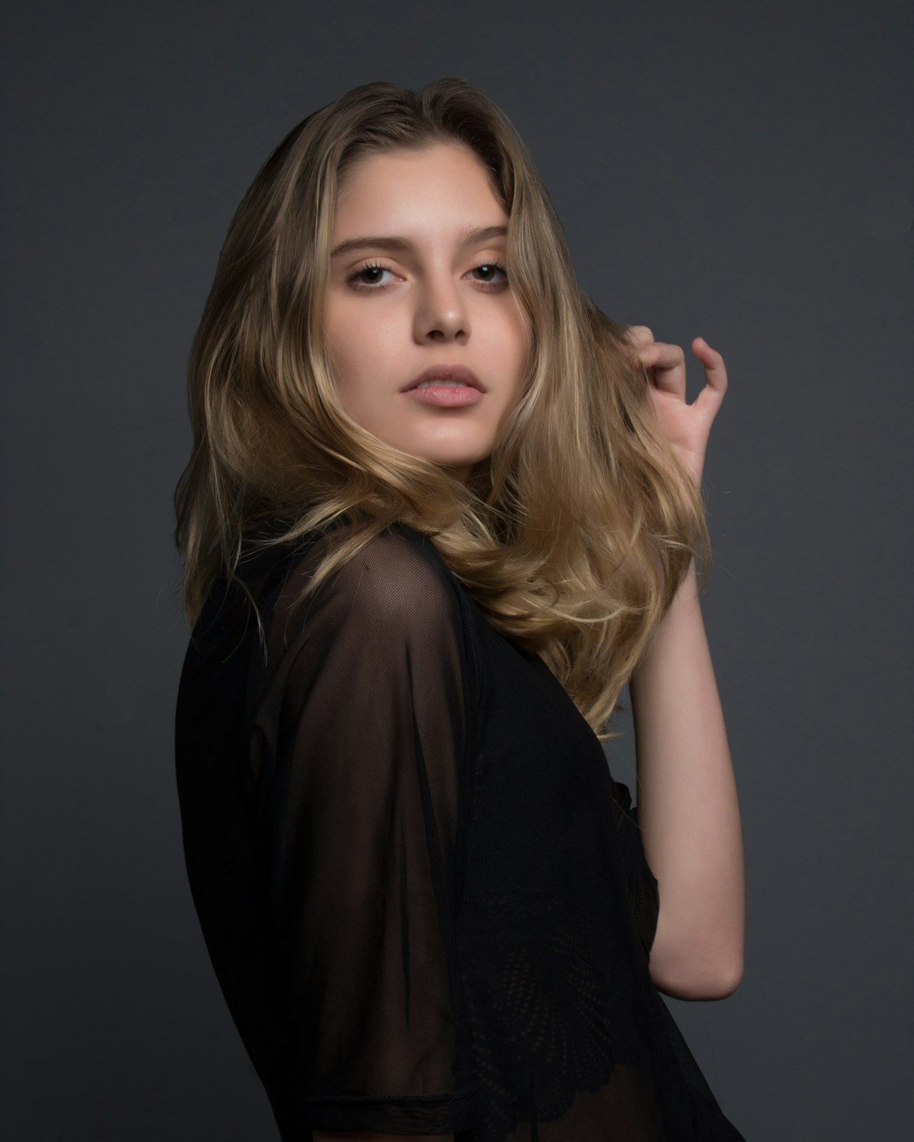 A studio beauty portrait, hair in motion, sheer black fabric on grey.
